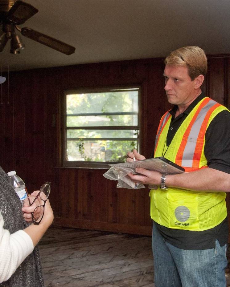 Inspector taking notes with a homeowner in a flood-damaged room