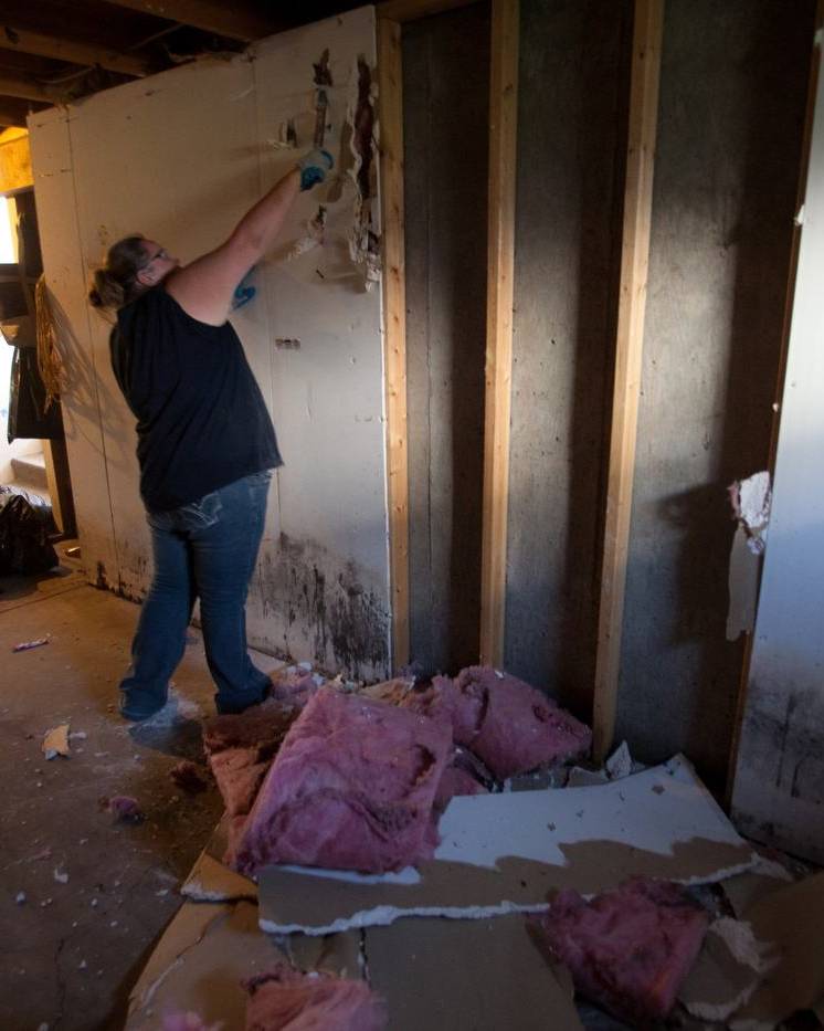 Worker cutting out moldy wall panels after a flood