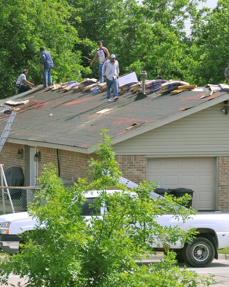 Roofing crew replacing shingles on a damaged house