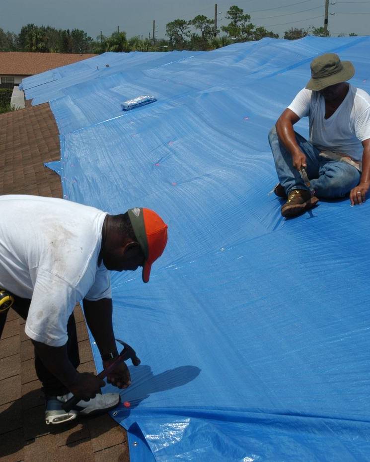 Workers covering a storm-damaged roof with a tarp